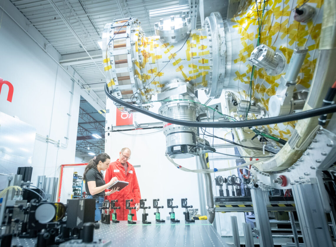 A photograph of a couple General Fusion employees reviewing some work with some innovative technology equipment in the foreground.